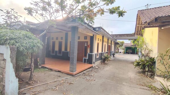 Una zona residencial con una casa que tiene un porche, un pequeño jardín y un sendero de tierra.