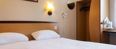 A hotel room with a bed, a wall-mounted lamp, a coat rack, and a mirror.