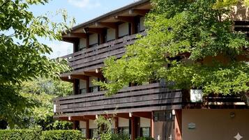 A multi-story building with balconies, surrounded by greenery.