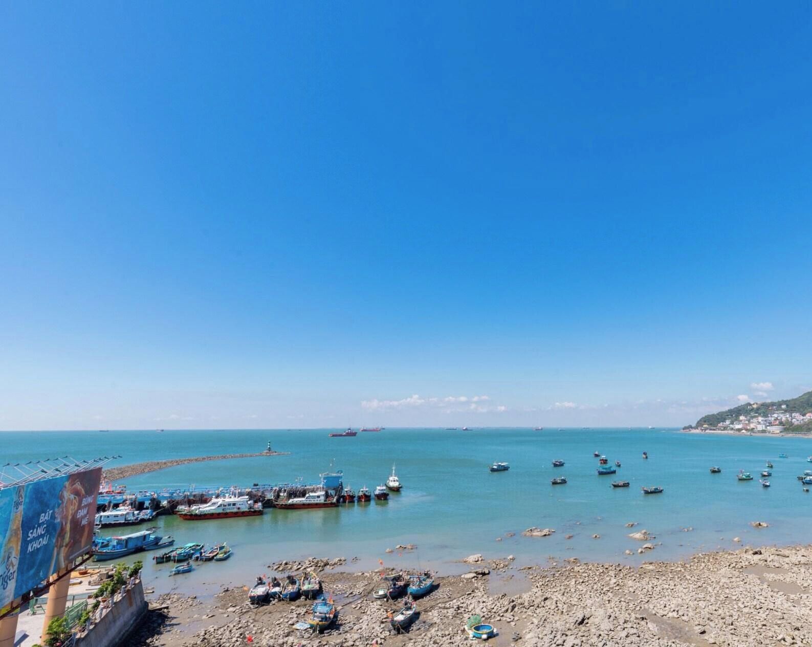 A coastal scene with boats docked at a pier, a rocky beach, and a clear blue sky.
