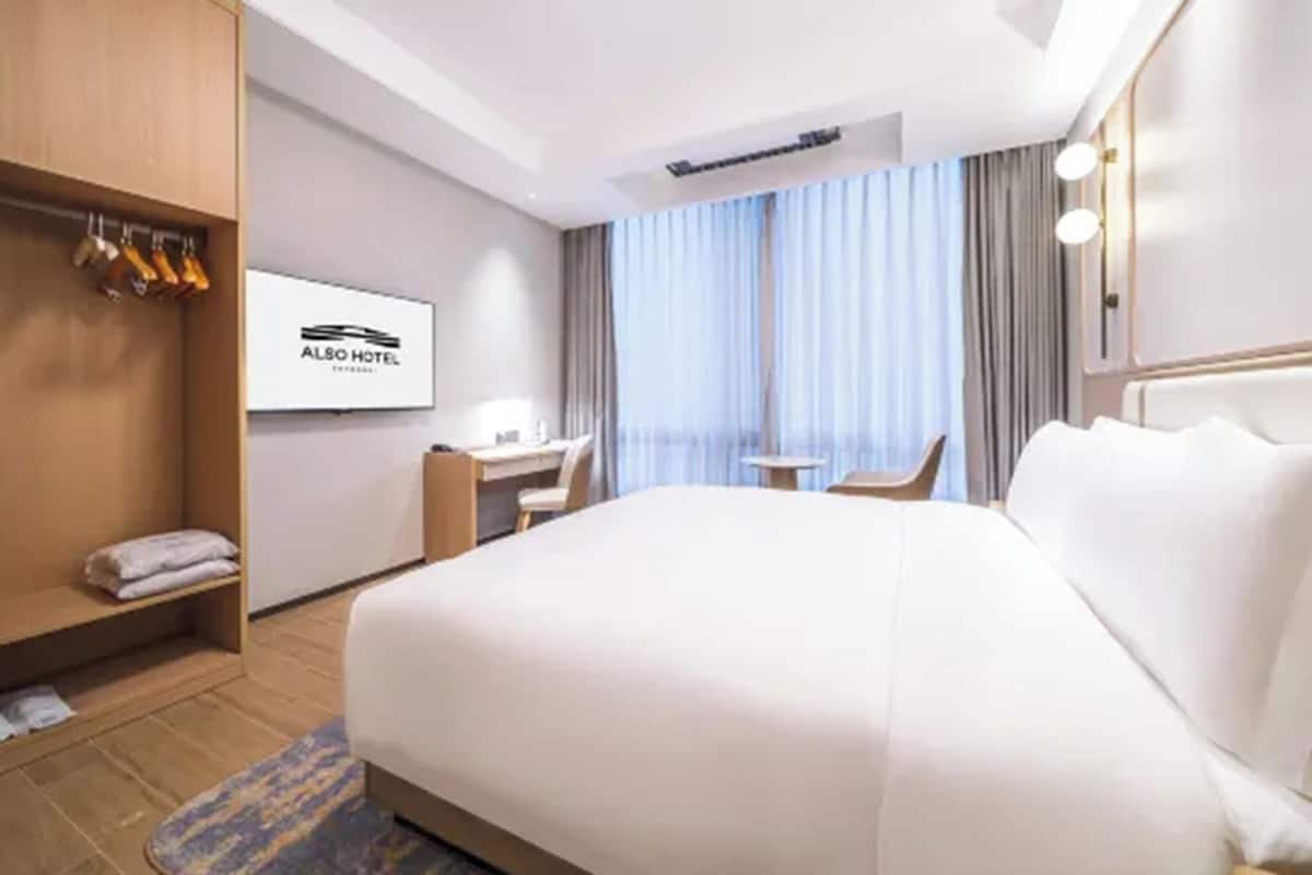 Hotellihuone, jossa on sänky, työpöytä, tuoli, vaatekaappi ja ikkuna, jossa on verhot.
