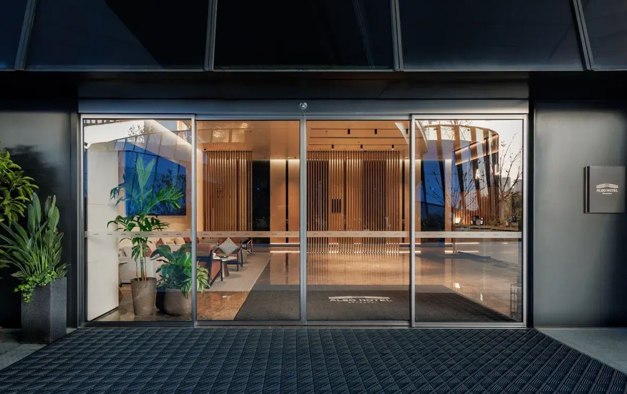 A hotel entrance with a glass door, interior seating, and potted plants.