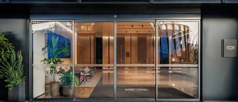 A hotel entrance with a glass door, interior seating, and potted plants.