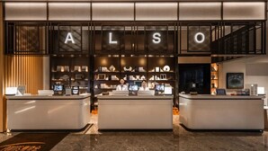 A hotel reception area with a modern design, featuring a large illuminated sign above the reception desk and a display of various items on shelves behind the staff. - Shanghai Also Hotel (Shanghai)