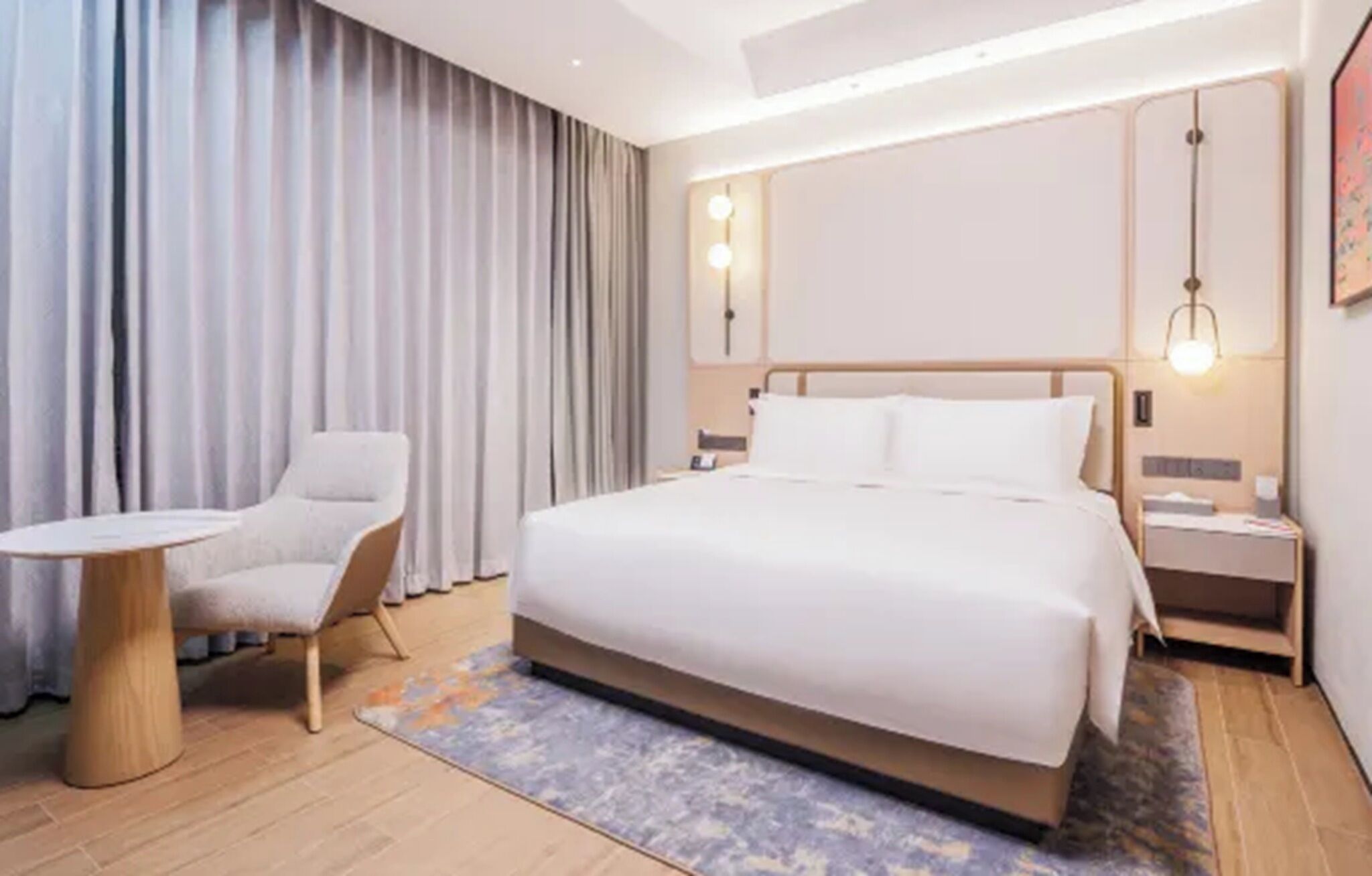 Moderni hotellihuone, jossa on suuri sänky, pieni pöytä, tuoli ja yöpöytä, jossa on lamppu.