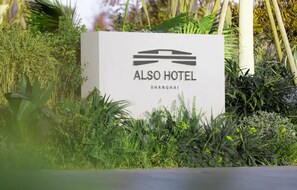 A sign for the ALSO HOTEL in SHANGHAI, surrounded by lush greenery. - Shanghai Also Hotel (Shanghai)