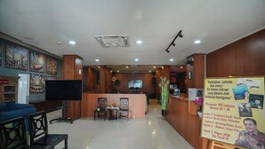 A reception area with a counter, seating, a television, and informational posters. - Mahakam24 Residence (Jakarta)
