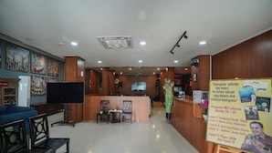 A reception area with a counter, seating, a television, and informational posters. - Mahakam24 Residence (Jakarta)