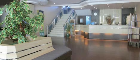 A lobby with a staircase, a reception desk, and a large potted plant.