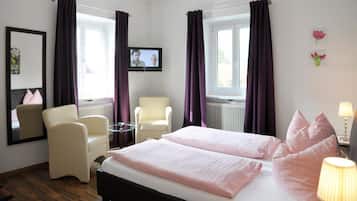 Una habitación de hotel con cama, dos sillas, una mesita, televisor y ventana con cortinas.