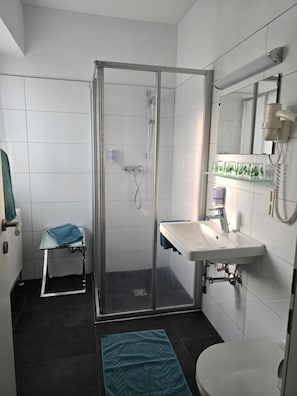 A modern bathroom with a glass shower enclosure, a white sink, a mirror, and a small table with a towel. - Hotel Hafnerwirt (Hallein)