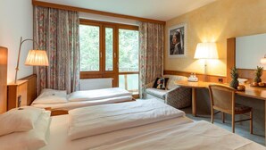 A hotel room with two beds, a desk with a chair, a window with curtains, a lamp, and a painting on the wall. - Hotel Restaurant Sv Drast Dreilv Ndereck (Arnoldstein)