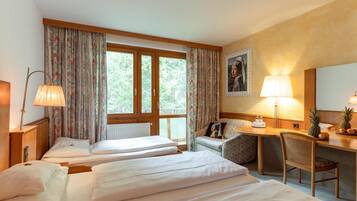 Quarto de hotel com duas camas, uma escrivaninha com cadeira, uma janela com cortinas, uma luminária e um quadro na parede.