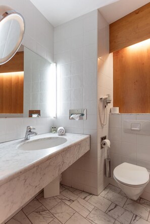 A modern bathroom with a marble sink, a mirror, a handheld showerhead, and a toilet. - Hotel Restaurant Sv Drast Dreilv Ndereck (Arnoldstein)