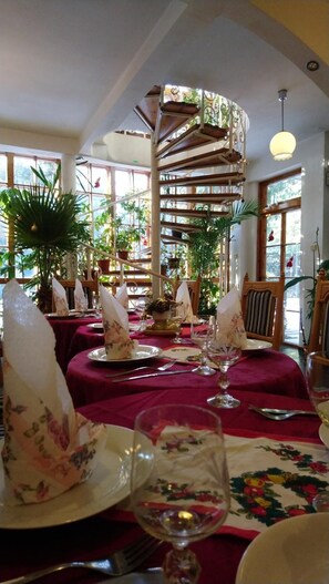 A dining area with tables set for a meal, surrounded by potted plants and a spiral staircase. - Park Hotel Amfora (Sofia)