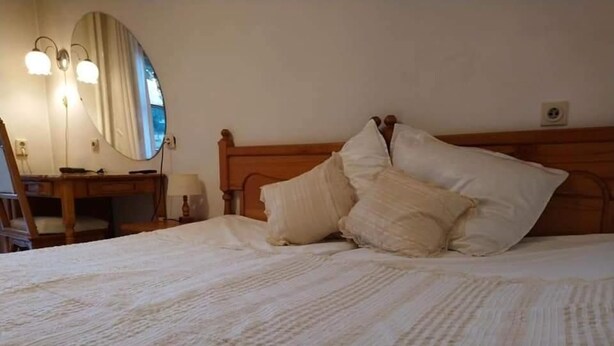 A neatly made bed with a wooden headboard, a bedside table with a lamp, and a mirror on the wall. - Park Hotel Amfora (Sofia)