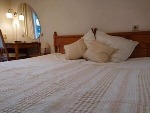 A neatly made bed with a wooden headboard, a bedside table with a lamp, and a mirror on the wall. - Park Hotel Amfora (Sofia)