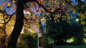 A garden with a tree, a pathway, and a building in the background. - Park Hotel Amfora (Sofia)