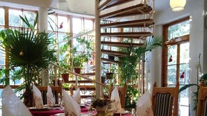 A dining area with tables set for a meal, surrounded by potted plants and a spiral staircase. - Park Hotel Amfora (Sofia)