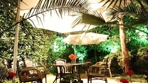 An outdoor seating area with a table and chairs under a large umbrella, surrounded by lush greenery. - Park Hotel Amfora (Sofia)