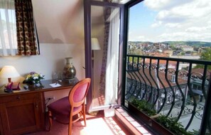 A balcony with a view of a town, a desk with a chair, and a vase with flowers. - Hotel Central (Veliko Tarnovo)
