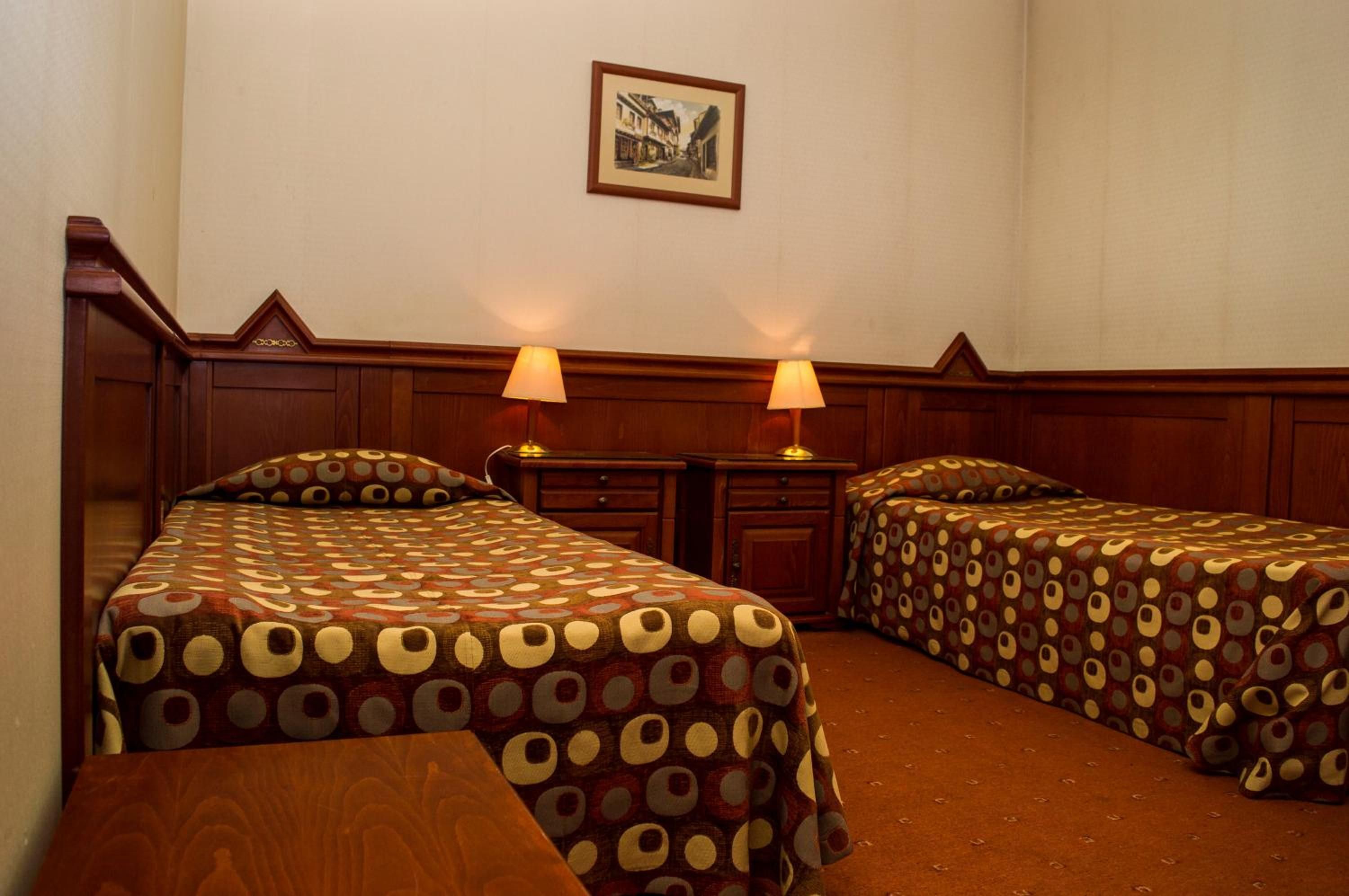 Habitación de hotel con dos camas, cabecera de madera, una mesita y dos lámparas de noche.
