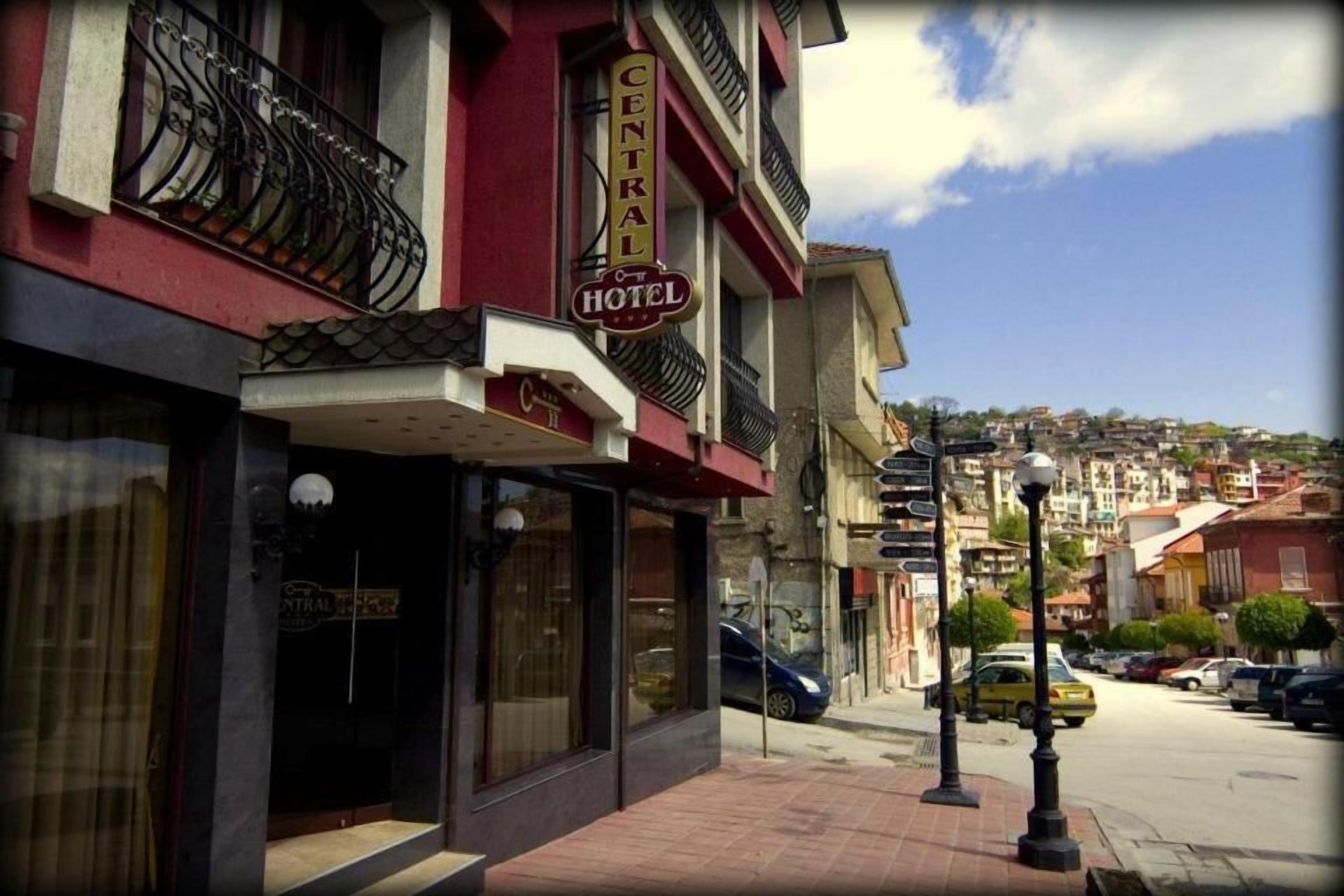 Un hotel con un letrero que dice 'CENTRAL HOTEL' en la fachada, vista de la calle con coches estacionados y cielo despejado.