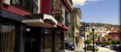 A hotel with a sign reading 'CENTRAL HOTEL' on the facade, a street view with parked cars, and a clear sky.