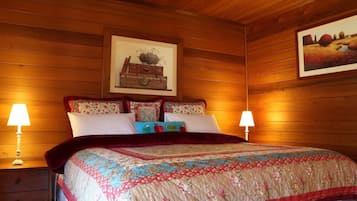 A wooden-paneled room with a bed, two bedside lamps, and two framed pictures on the walls.