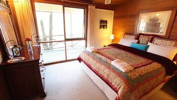 A bedroom with a large bed, a nightstand, a dresser, a window with curtains, and a ceiling fan.