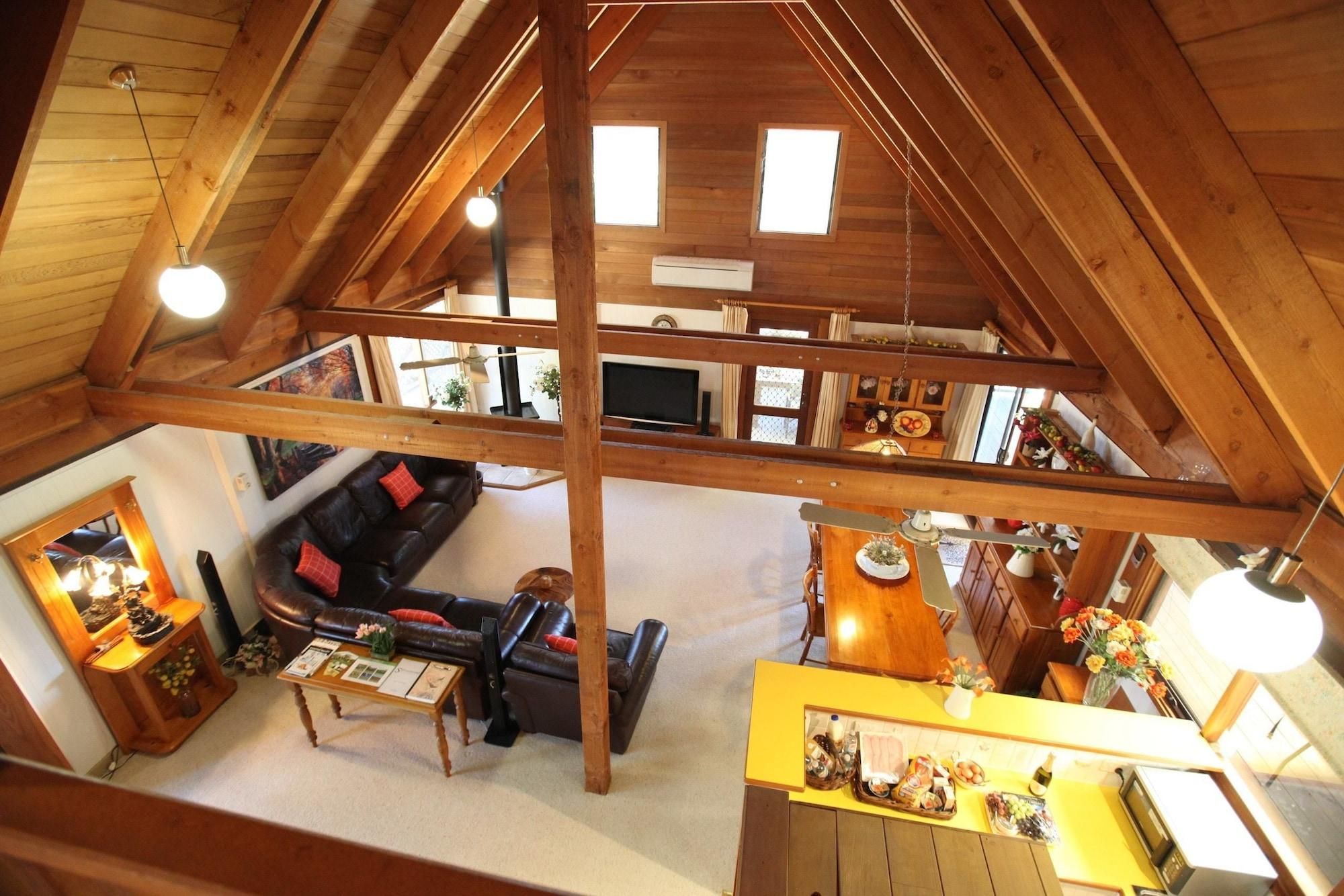 A loft-style room with a high ceiling, exposed wooden beams, a sofa, a dining table, and a kitchen area.