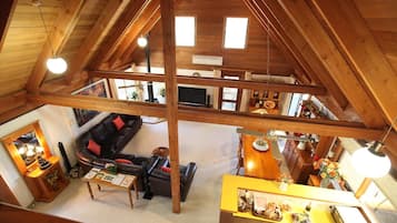 A loft-style room with a high ceiling, exposed wooden beams, a sofa, a dining table, and a kitchen area.
