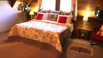 A cozy bedroom with a wooden ceiling, a floral bedspread, a bedside table with a lamp, and a small rug with a tree design.