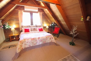 Un accogliente sottotetto adibito a camera da letto, con un letto, una poltrona e un piccolo addobbo a forma di albero.