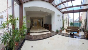 Un vestíbulo amplio con techo de vidrio curvo, una recepción y una zona de estar con sofá.