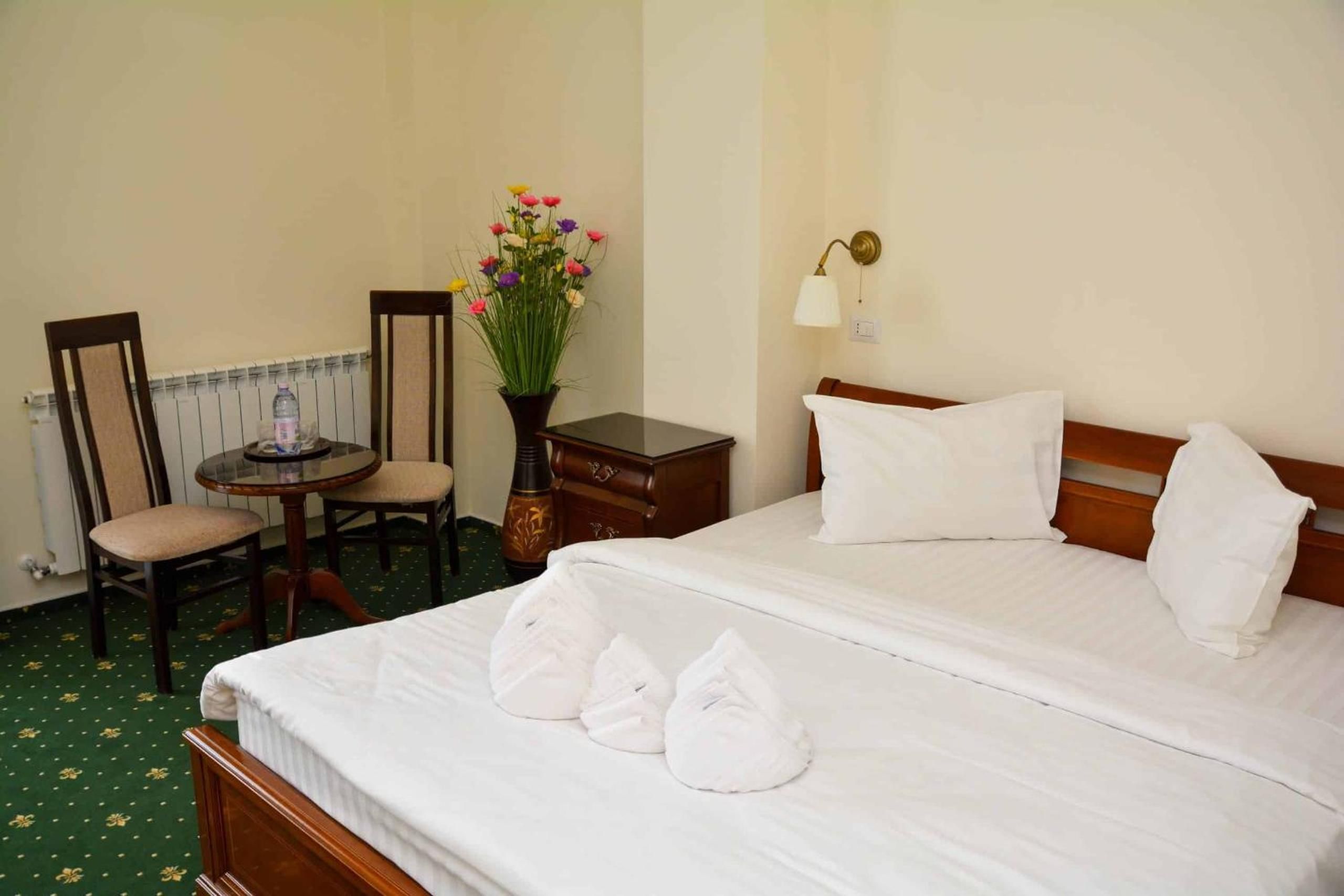 Habitación de hotel con cama, dos sillones, una mesita, un florero con flores y una lámpara de noche.