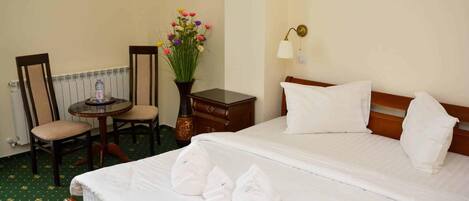 Habitación de hotel con cama, dos sillones, una mesita, un florero con flores y una lámpara de noche.