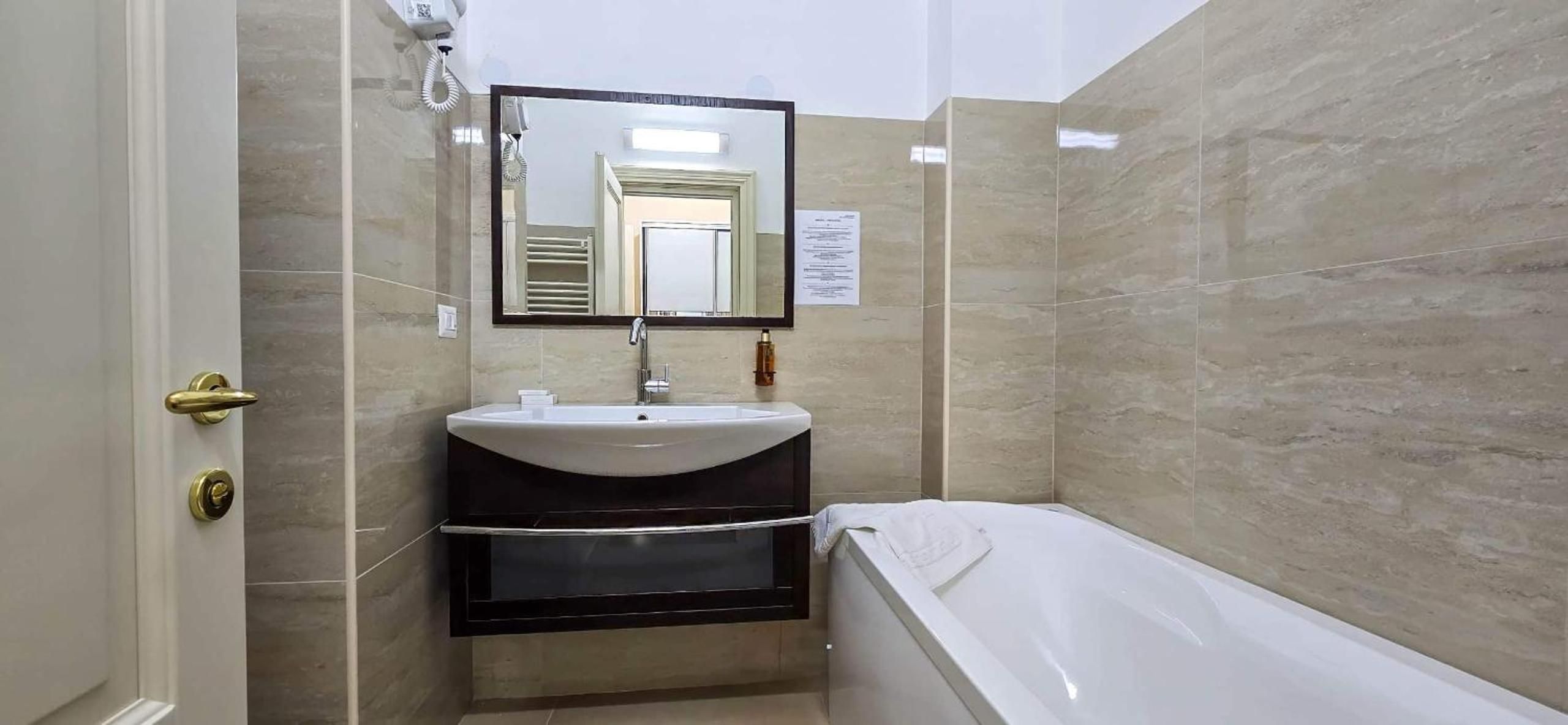 Un baño con una bañera blanca, un lavabo con espejo y una toalla colgada en la pared.