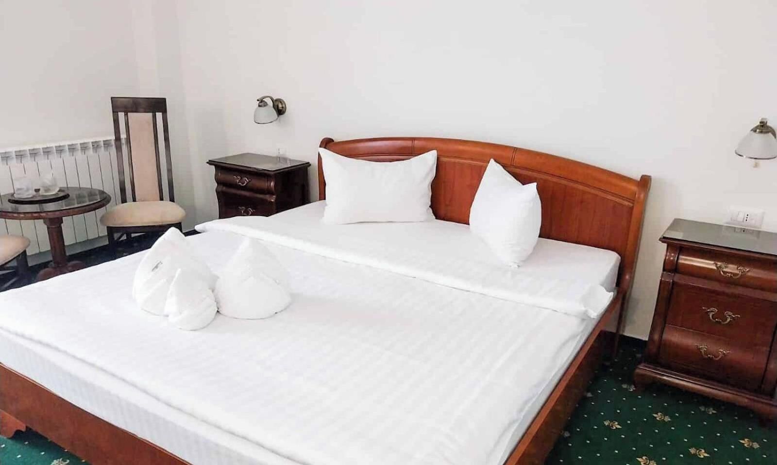 A neatly made bed with pillows and a blanket, a bedside table, a lamp, and a chair in a hotel room.