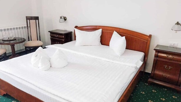 Una cama bien hecha con almohadas y una manta, una mesita de noche, una lámpara y una silla en una habitación de hotel.