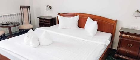 A neatly made bed with pillows and a blanket, a bedside table, a lamp, and a chair in a hotel room.