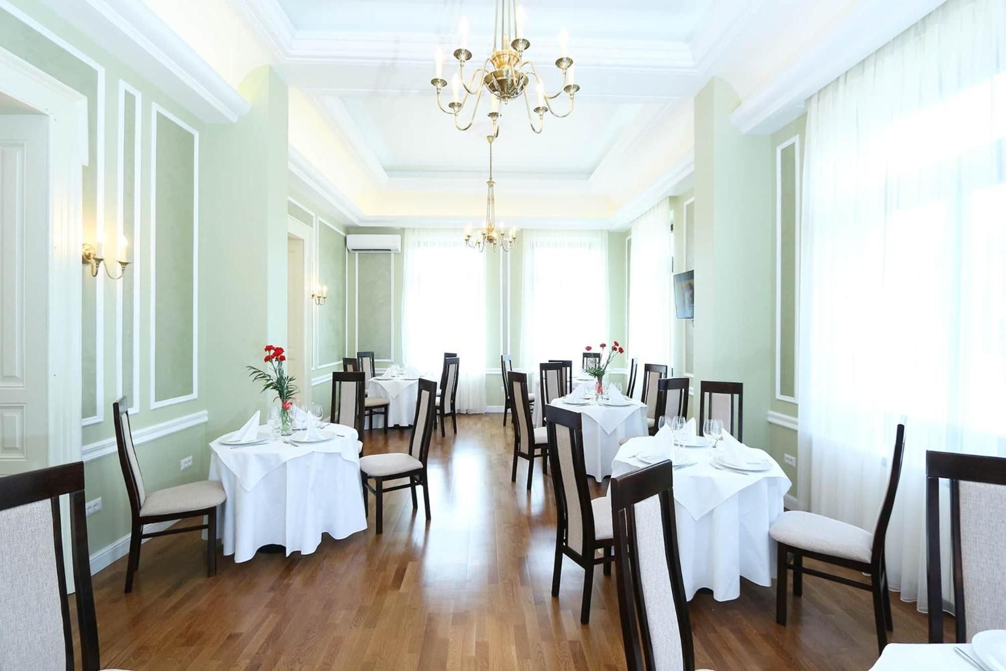 Un comedor con varias mesas y sillas, una araña y paredes de colores claros.