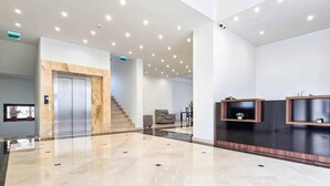Un vestíbulo moderno con suelo de mármol, una escalera y un mostrador de recepción con televisor de pantalla plana.