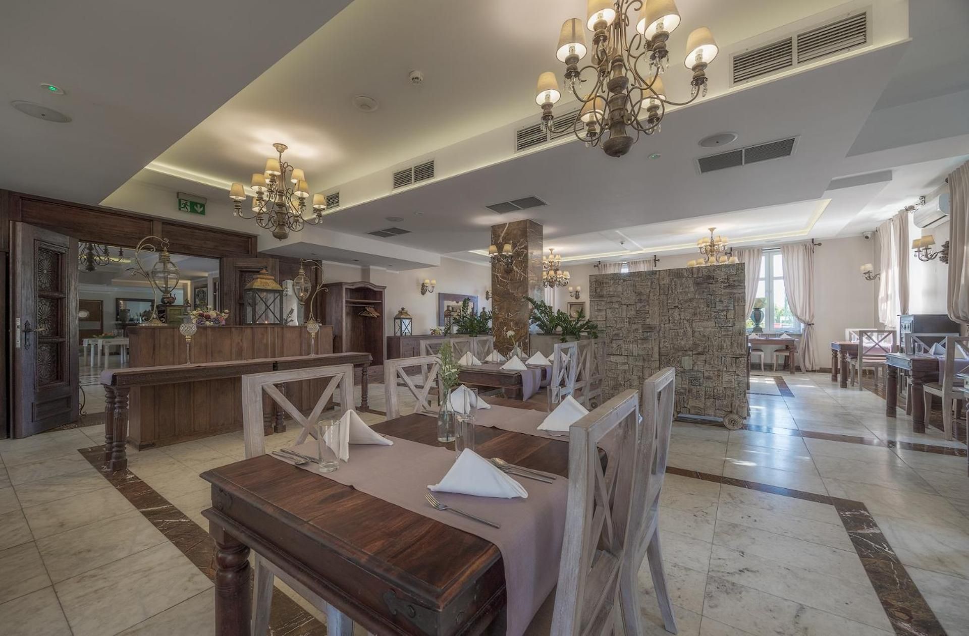 A spacious hotel lobby with a reception desk, multiple dining tables, and a stone accent wall.