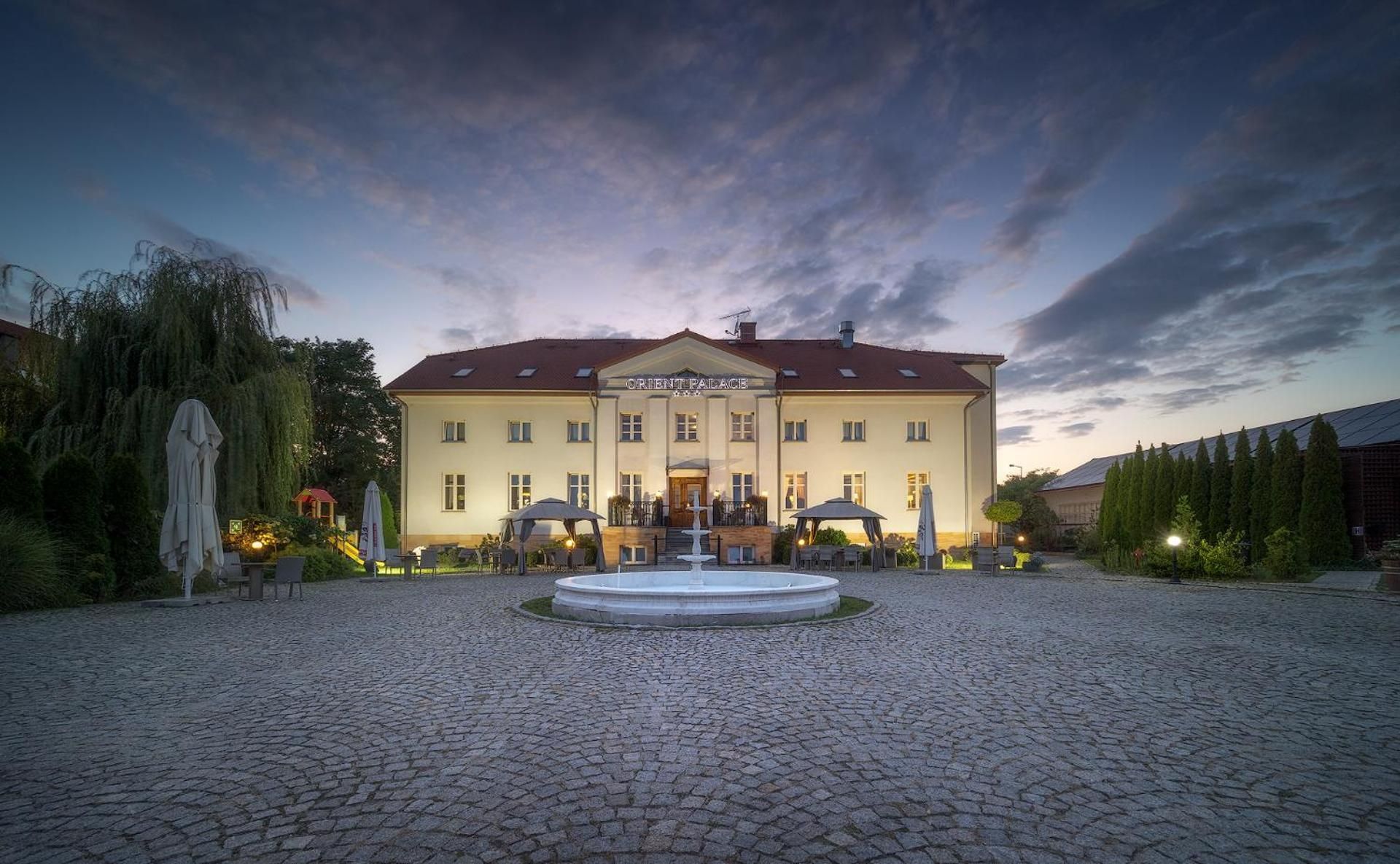 Ein großes Gebäude mit einer zentralen Fontäne, umgeben von einem Kopfsteinpflasterhof.