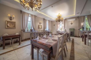 A dining area with multiple tables set for service, chandeliers, and a view of greenery outside. - Orient Palace (Kobierzyce)