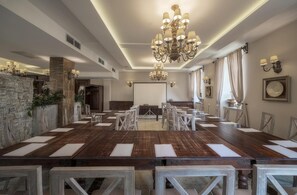 A conference room with a long table, chairs, a chandelier, stone wall, and a projector screen. - Orient Palace (Kobierzyce)
