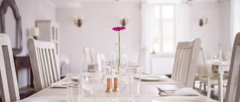 A dining table set with white plates, glasses, and cutlery, with a single flower centerpiece.