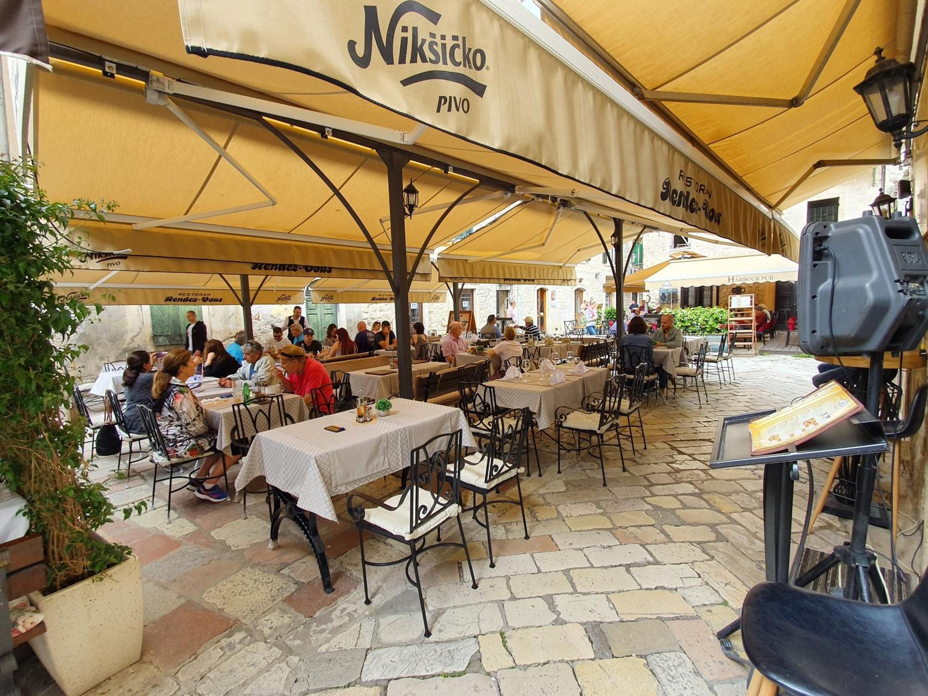 An outdoor café area with tables and chairs under yellow umbrellas, some with menus and drinks.