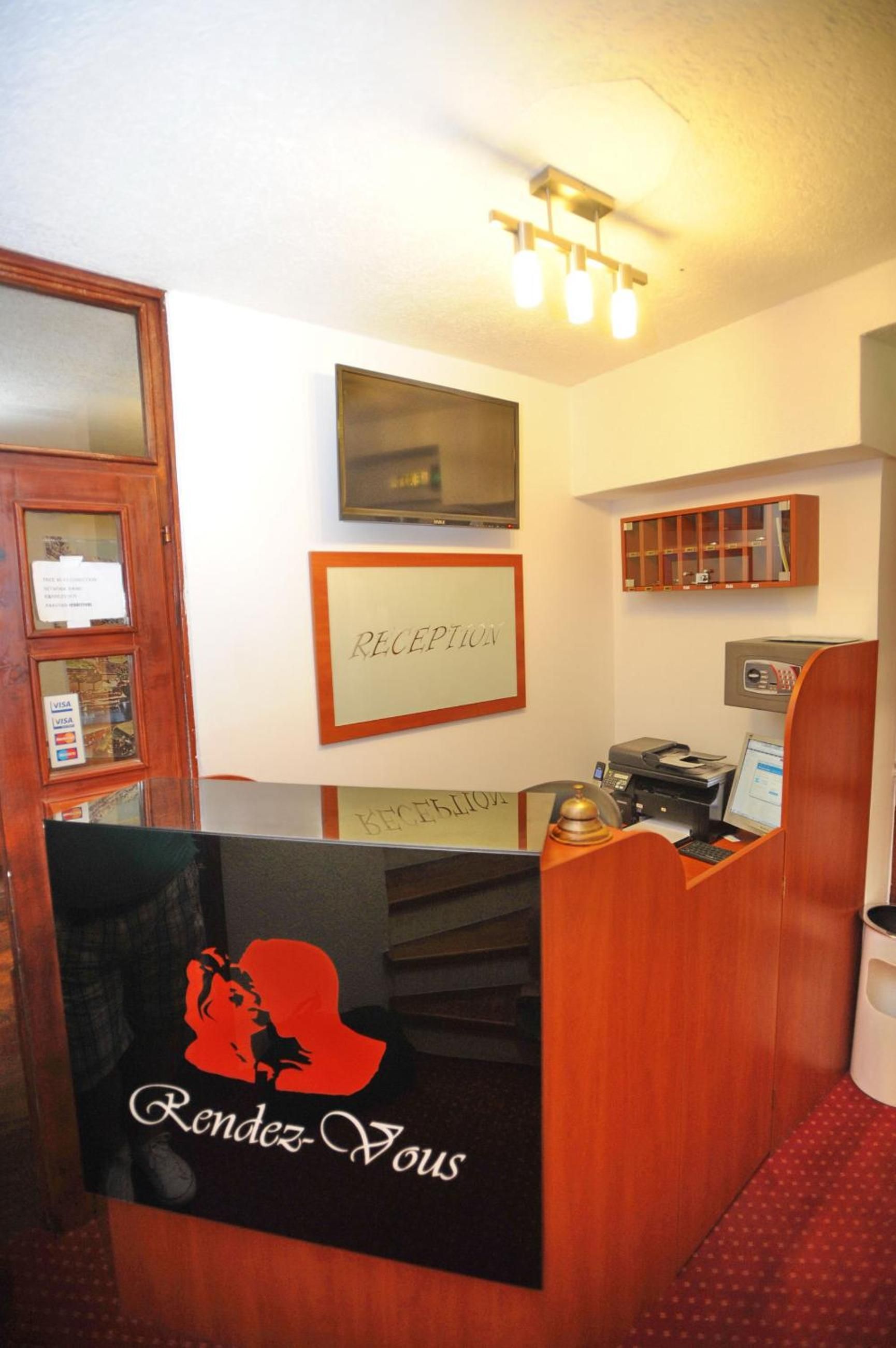 Ein Empfangsschalter mit einem 'RECEPTION'-Schild darüber, ein Holzkabinett, ein an der Wand befestigter Fernseher und ein Computer auf dem Schalter.